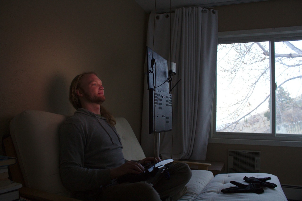 photo of laptop suspended in front of face, sitting on futon