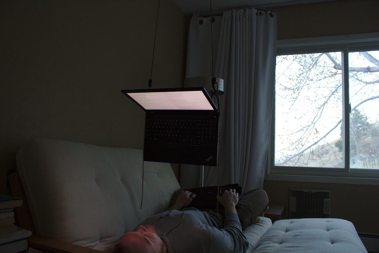 photo of laptop suspended above face, laying on futon